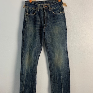 Puede incluir: Un par de pantalones vaqueros azules de mezclilla con un aspecto descolorido y desgastado. Los vaqueros tienen una pierna recta y un diseño clásico de cinco bolsillos.