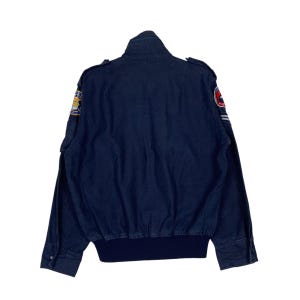May include: Navy blue bomber jacket with a ribbed hem and cuffs. The jacket features patches on the sleeves and shoulders. The jacket has a stand-up collar and buttoned cuffs. The back of the jacket is visible.