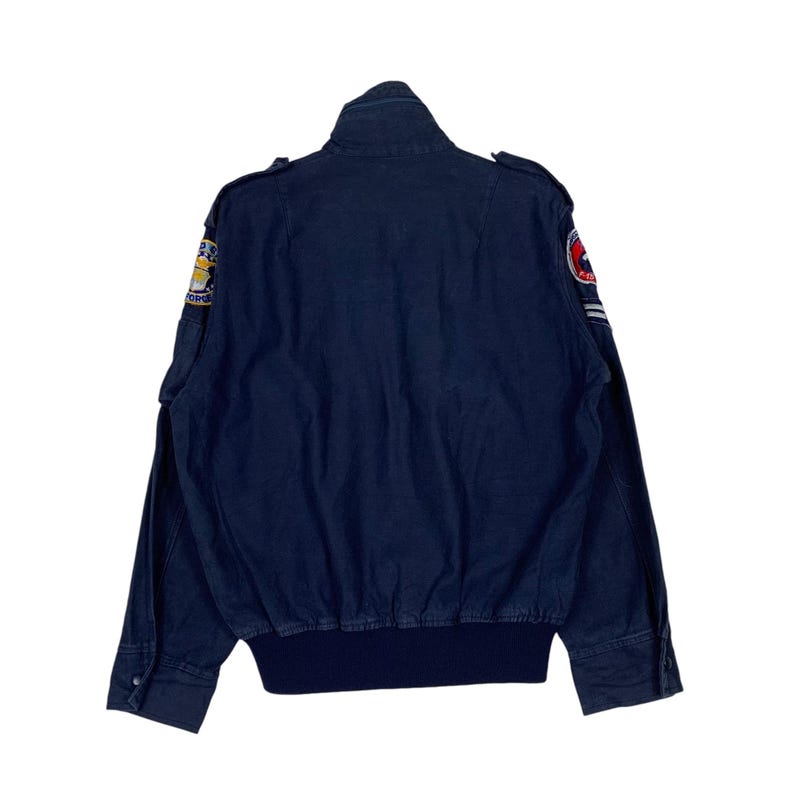 May include: Navy blue bomber jacket with a ribbed hem and cuffs. The jacket features patches on the sleeves and shoulders. The jacket has a stand-up collar and buttoned cuffs. The back of the jacket is visible.