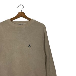 May include: A beige long-sleeved sweatshirt with a small black graphic on the front.
