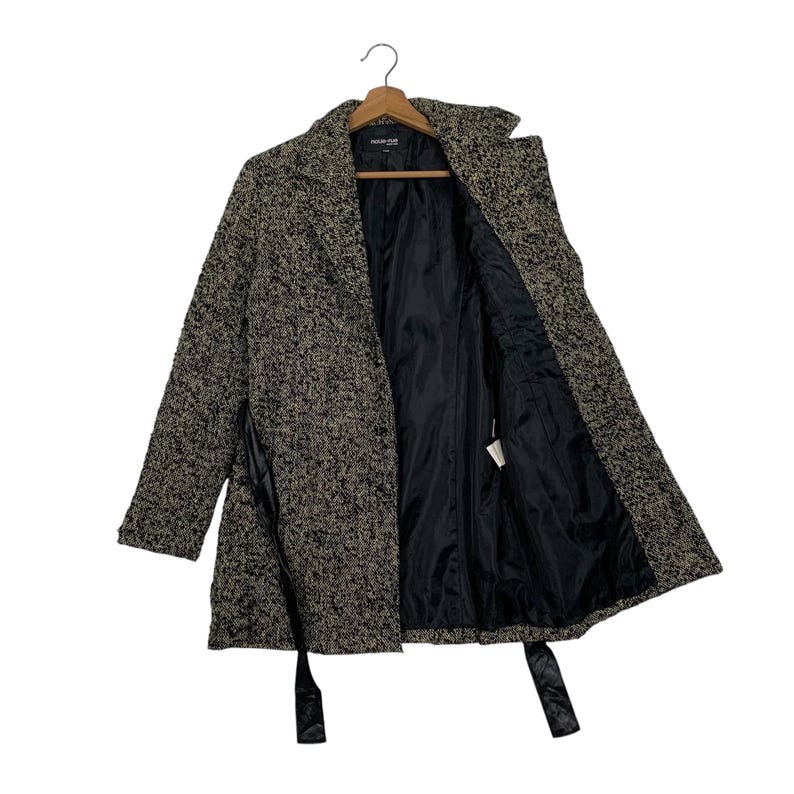 Puede incluir: Un abrigo de estilo tweed en tonos marrones y negros, colgado de una percha de madera. El abrigo presenta un cuello con muescas, un forro de sat&eacute;n negro y un cintur&oacute;n a juego. El abrigo est&aacute; abierto, revelando el forro interior y una etiqueta.