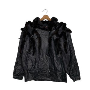 May include: Black leather jacket with fur trim. The jacket features a button-up front, a collar with fur trim, and decorative fur accents. The jacket is hanging on a wooden hanger. The leather appears to be slightly distressed.
