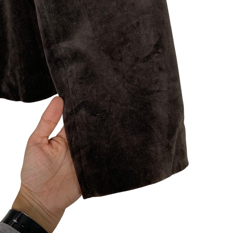 Peut inclure: Gros plan sur une manche de blazer marron fonc&eacute;. Le tissu semble &ecirc;tre une mati&egrave;re douce et velout&eacute;e. La manche est tenue par une main, montrant la texture et la couleur du v&ecirc;tement. Le blazer est de couleur unie.