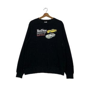 Könnte beinhalten: Schwarzer Langarm-Pullover mit einem weißen und roten Aufdruck von zwei Autos und dem Text "RedSuns RX-7" mit den Worten "Atsuko Takahashi,  Apprentice Takahashi" darunter.