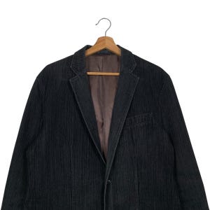 May include: A dark gray corduroy blazer with a single button closure. The blazer has a striped pattern and a classic fit.