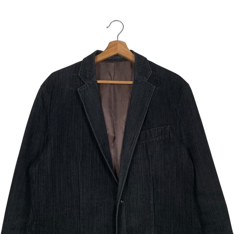 May include: A dark gray corduroy blazer with a single button closure. The blazer has a striped pattern and a classic fit.