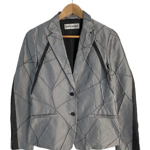 May include: A grey blazer with a geometric pattern and black trim on the sleeves. The blazer has a two-button closure and the label "ISSEY MIYAKE" is visible on the inside.