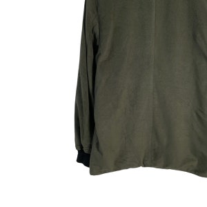 May include: A long-sleeved, dark green shirt with a black ribbed cuff. The shirt is made of a soft, textured fabric.