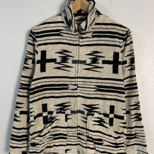 Puede incluir: Una chaqueta con cremallera y cuello alto con estampado en blanco y negro. La chaqueta tiene un dise&ntilde;o geom&eacute;trico con rayas y cruces en blanco y negro.