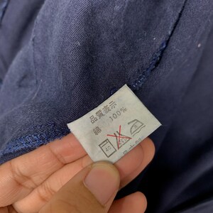 May include: Close-up of a navy blue garment with a white tag. The tag has Japanese text and symbols, including "100%" and washing instructions. The garment's fabric is visible in the background.