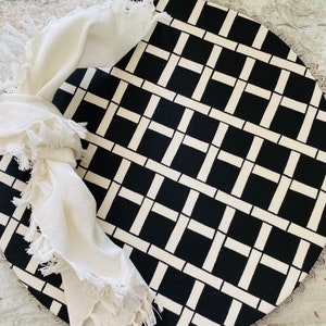 May include: A round black and white placemat with a geometric pattern. The placemat has a fringed white napkin on top.