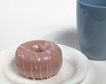 May include: A pink donut with white frosting and a white glaze drizzled over the top. The donut is on a white plate.