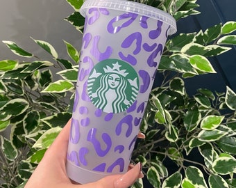 May include: A clear plastic reusable cup with a purple leopard print design and the Starbucks logo.