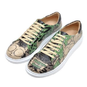 Puede incluir: Un par de zapatillas bajas con suela blanca y parte superior verde, negra y beige. La parte superior presenta un gráfico de dibujos animados con el texto "Everyone needs something they can not survive without".