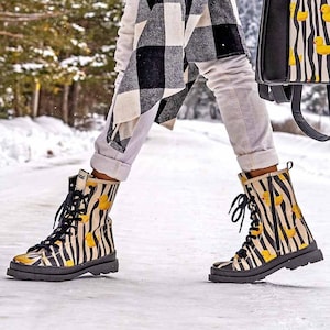 May include: Black and white striped boots with yellow rubber duckies printed on them. The boots are lace-up and have a thick black sole.