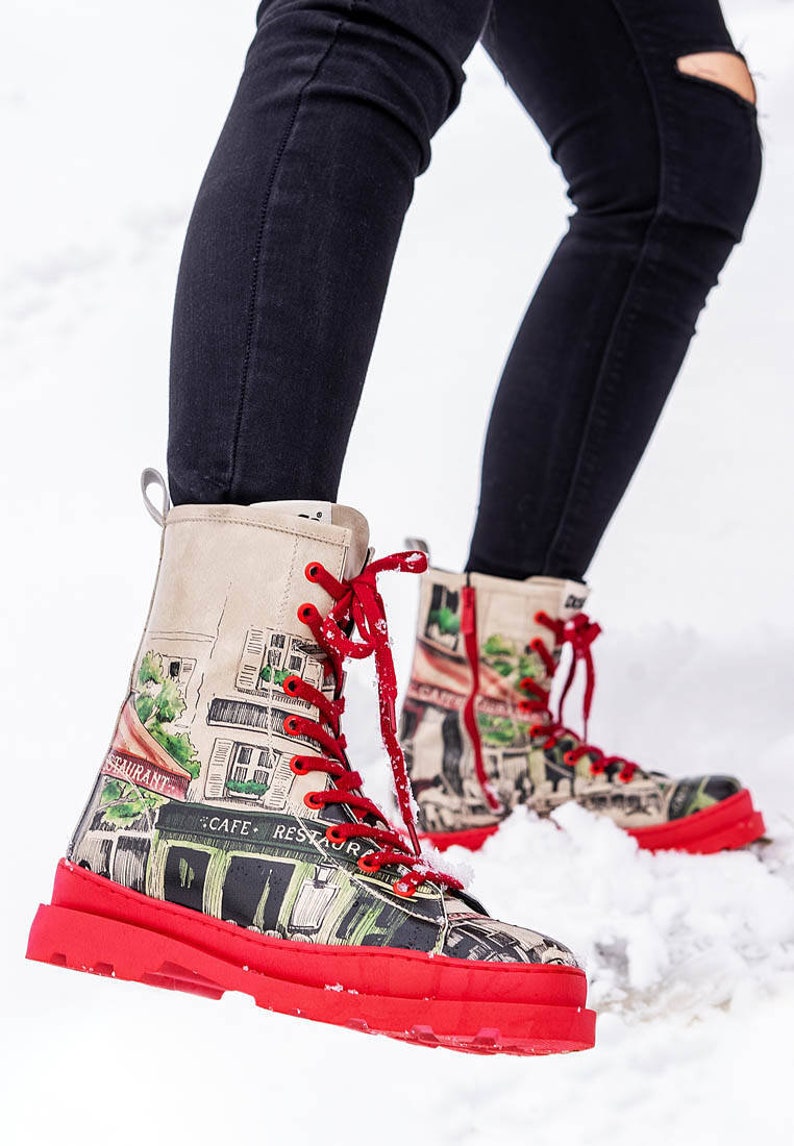 May include: Red and white high-top boots with a graphic print of a Parisian street scene. The boots have red laces and a thick red sole.