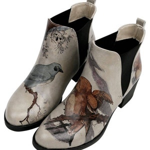 May include: A pair of gray ankle boots with a bird print design. The boots have a black elastic panel on the back and a low block heel.