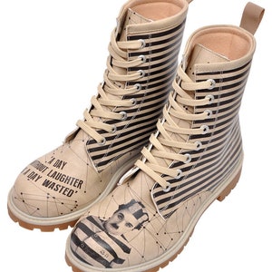 Könnte beinhalten: Ein Paar beige und schwarz gestreifte Schnürstiefel mit weißer Sohle. Die Stiefel zeigen ein gedrucktes Bild von Charlie Chaplin in einem gestreiften Häftlingsoutfit. Der Text "A DAY WITHOUT LAUGHTER IS A DAY WASTED" ist auf den Stiefeln gedruckt.