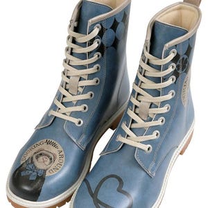 May include: A pair of blue lace-up boots featuring a graphic of a ferret wearing a blue bow tie on the toe with the text Dooking Around. The boots have beige laces, a beige pull tab at the heel, a white midsole, and a brown lugged rubber outsole.