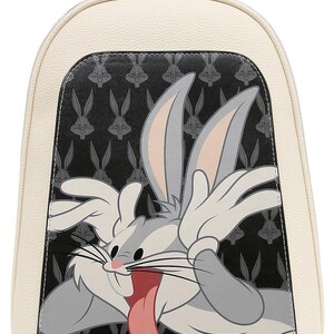 May include: A cream-colored backpack featuring a black front panel with a repeating Bugs Bunny head pattern. A large, colorful graphic of Bugs Bunny with long ears, white gloves, and a pink tongue sticking out is centered on the front of the bag.
