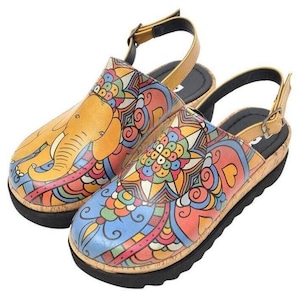May include: A pair of colorful clogs with a cork sole and black rubber bottom. The clogs feature a vibrant, hand-painted design with an elephant and floral patterns in shades of yellow, blue, red, and green. The adjustable strap is a light brown color.