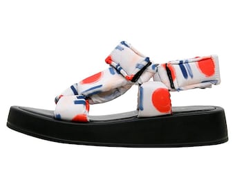 May include: White platform sandals with red and blue abstract print. The sandals have a thick black platform sole and adjustable straps.