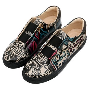 May include: A pair of black canvas slip-on shoes with a white background and colorful graphic print. The print includes the words "Ludwig Frank" and "Schames".