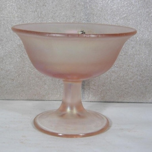 May include: A vintage pink glass dessert bowl with a stem. The bowl has a rounded shape with a flared rim and sits on a short, pedestal-style base. The glass has a frosted appearance.