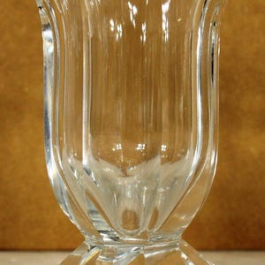 May include: A clear glass vase with a tulip-shaped design. The vase has a flared top and a faceted base. The glass is transparent, allowing light to pass through, and the vase is likely used for displaying flowers.