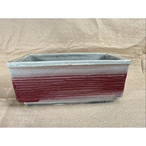 May include: Rectangular ceramic planter with a grey rim and a textured, burgundy-coloured body. The planter has a rectangular shape and is suitable for indoor or outdoor use. The planter is approximately 30 cm long.