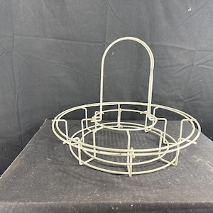 May include: Off-white metal wire egg basket with a circular base and a handle. The basket has a series of vertical dividers and a handle that arches over the top. The basket is designed to hold eggs.