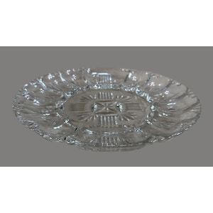 Op de afbeelding: Transparante glazen serveerschaal met een geschulpte rand. Het midden van de schaal heeft een geometrisch sterrenpatroon. De schaal is rond en heeft een iets verhoogde basis. Ideaal voor het serveren van hapjes of desserts.