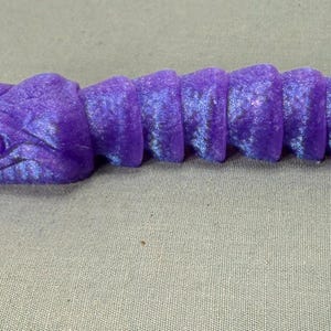 May include: A purple snake-shaped keyring with a silver key ring. The snake has a detailed head and segmented body, with a gradient of purple and blue hues. The keyring is made of a 3D-printed material.