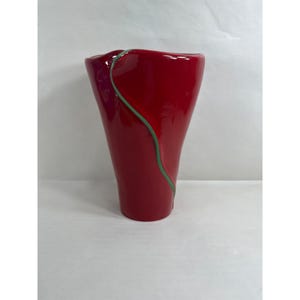 Może przedstawiać: Wysoki, czerwony wazon z błyszczącym wykończeniem. Cienka, zielona, zakrzywiona linia akcentuje bok wazonu. Wazon ma lekko rozszerzoną górę i gładki, zakrzywiony kształt. Wazon jest pusty i stoi na białej powierzchni.