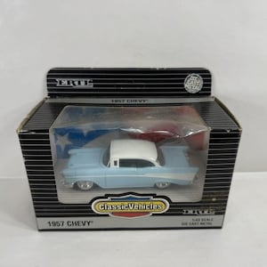 May include: A die-cast metal 1957 Chevy model car in a box. The car is light blue with a white roof. The box is black with white stripes and the text "1957 Chevy" and "Classic Vehicles".