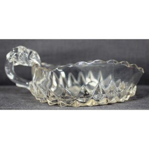 May include: A clear glass dish with a decorative handle. The dish has a scalloped edge and a diamond pattern.