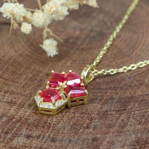 May include: A gold necklace with a pendant featuring three red ruby stones set in gold with a halo of small clear diamonds.