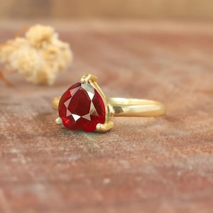 Könnte beinhalten: Ein goldener Ring mit einem herzförmigen roten Edelstein.