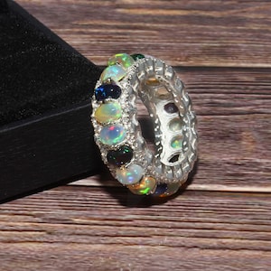 Könnte beinhalten: Ein silberner Ring mit einer Reihe kleiner weißer Steine und einer Reihe bunter Opal-Steine.