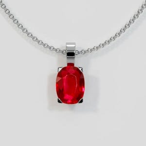 May include: A silver chain necklace with a pendant featuring a large, oval-shaped, red gemstone.