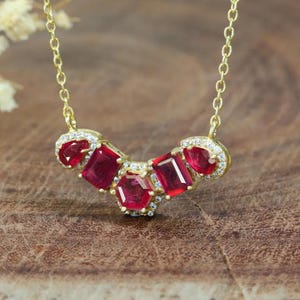 Könnte beinhalten: Eine goldene Kettenkette mit einem Anhänger mit fünf roten Edelsteinen, die von kleineren klaren Edelsteinen umgeben sind.