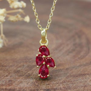 Puede incluir: Un collar de cadena de oro con un colgante que presenta un grupo de cinco piedras preciosas rojas en forma de pera.