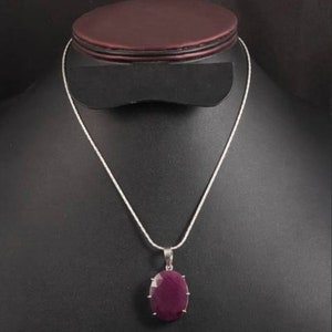 Puede incluir: Un collar de cadena de plata con un colgante que presenta una piedra preciosa grande, de forma ovalada, de color púrpura oscuro.