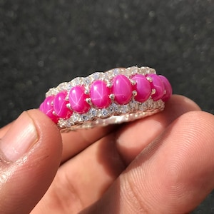 Könnte beinhalten: Ein Silberring mit einer Reihe von rosa Stern-Saphiren und kleineren klaren Steinen.