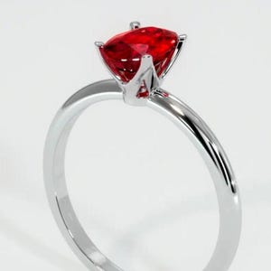 Könnte beinhalten: Ein silberner Ring mit einem roten Edelstein in einer Krappenfassung.