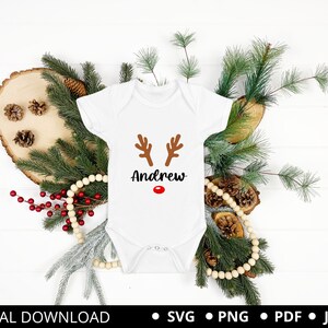 May include: White onesie with a brown reindeer face and red nose. The onesie has the name "Andrew" printed on it.