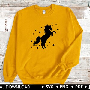 Puede incluir: Una sudadera amarilla con una silueta negra de un unicornio con un dise&ntilde;o de estrellas.