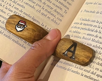 May include: Two wooden bookmarks, one with a Santa Claus illustration and the other with the letter "A" in black lettering. The bookmarks are on a book with text about sleep cycles.