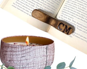 May include: A wooden bookmark with the initials "CM" engraved on it. The bookmark is resting on a book with a lit candle in front of it. The candle is in a white and brown ceramic container with a wood grain pattern.