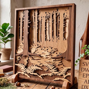 May include: A detailed wooden forest scene, laser-cut with multiple layers to create a 3D effect. The artwork depicts trees, ferns, and foliage, set within a dark brown frame. A small wooden sign displays "SVG DWG EPS AI DXF".
